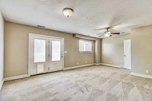 Spacious room featuring neutral carpeting, a ceiling fan with integrated lighting, and a double-door exterior entry with an integrated pet door