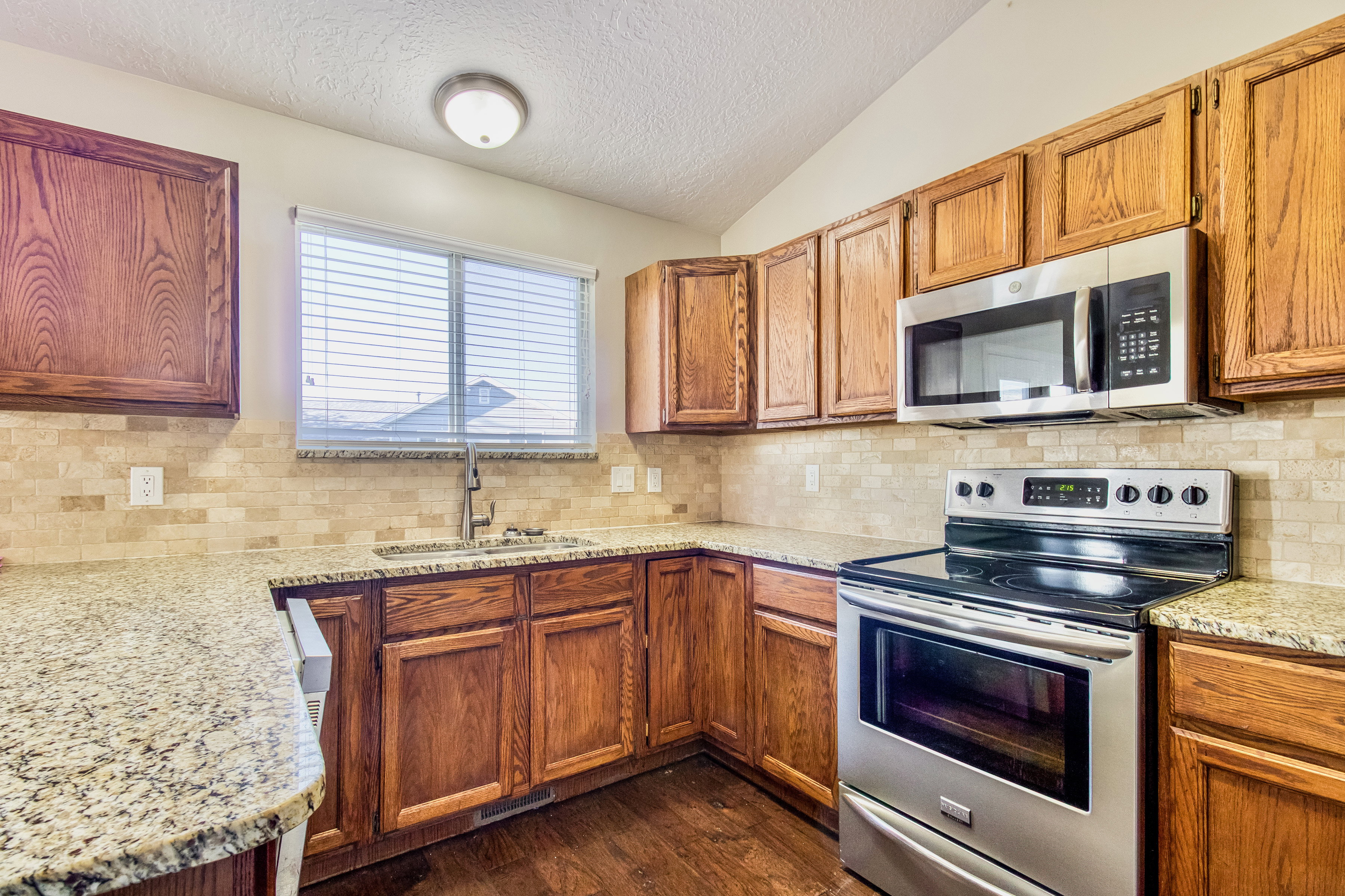 Kitchen featuring wood cabinetry, light-toned granite countertops, and a tiled backsplash