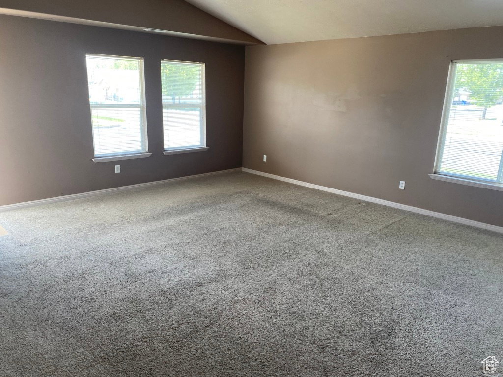 Spacious living room featuring vaulted ceilings, light brown carpeting, and multiple windows with white trim