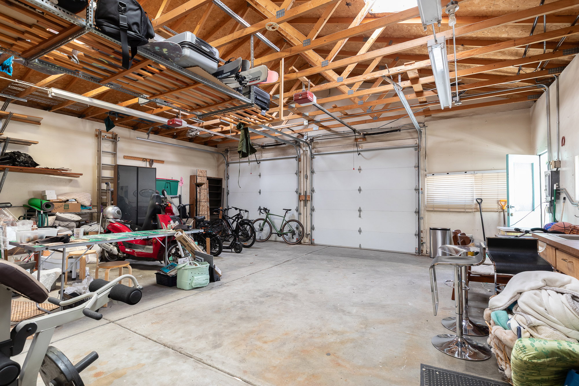 Spacious garage featuring exposed wood beam ceilings, two large roll-up doors, concrete flooring, and built-in shelving