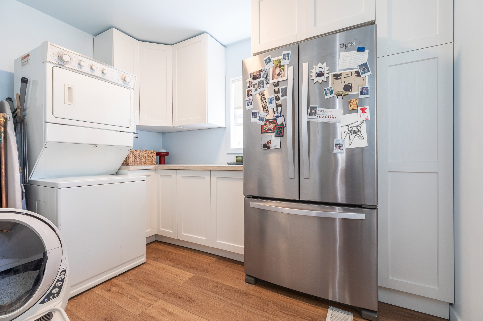 Kitchen featuring wood-finish flooring, white shaker-style cabinetry, light countertops, and a stainless steel refrigerator