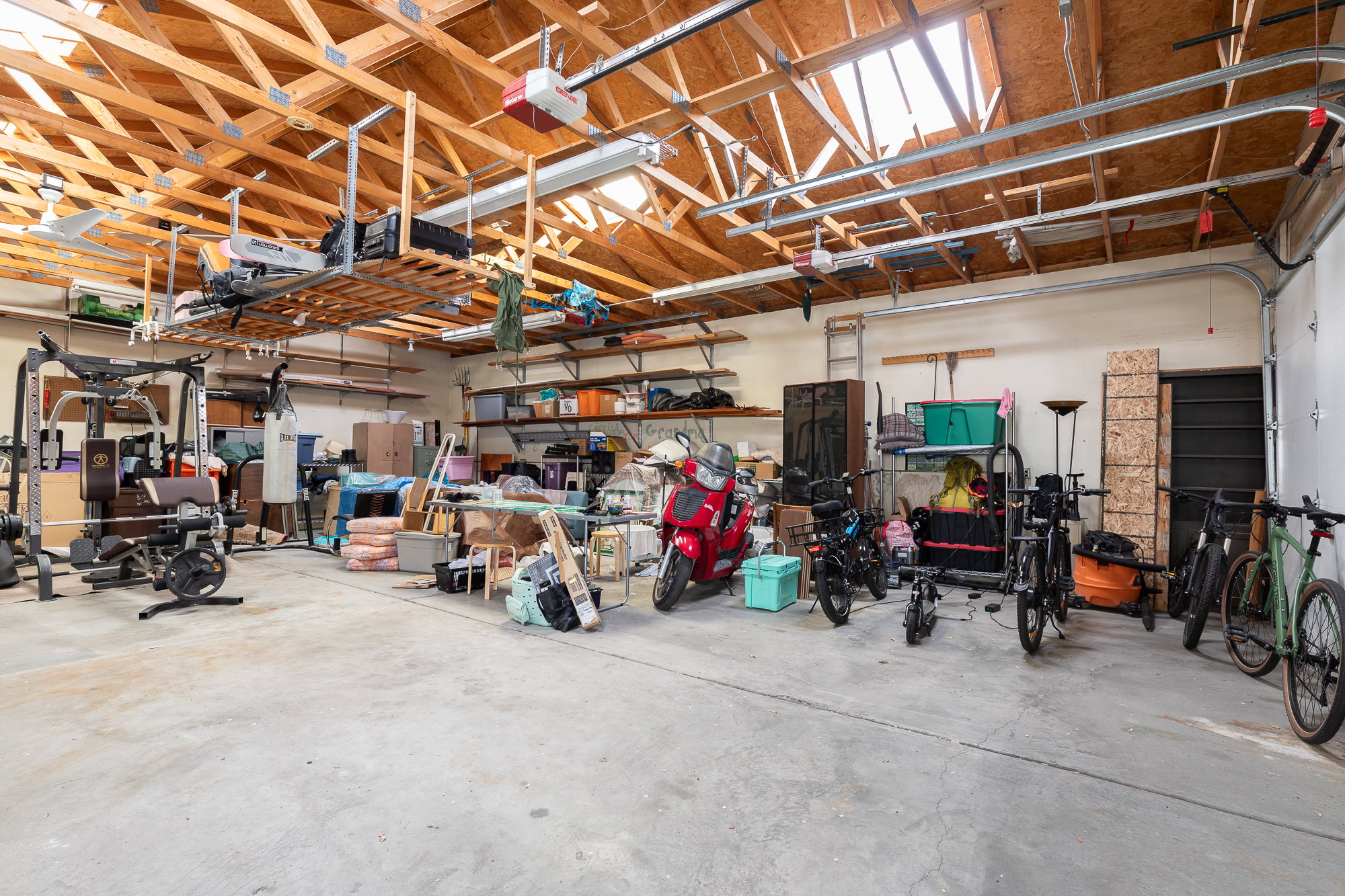Spacious garage featuring an exposed beam ceiling, concrete flooring, skylights, and built-in shelving