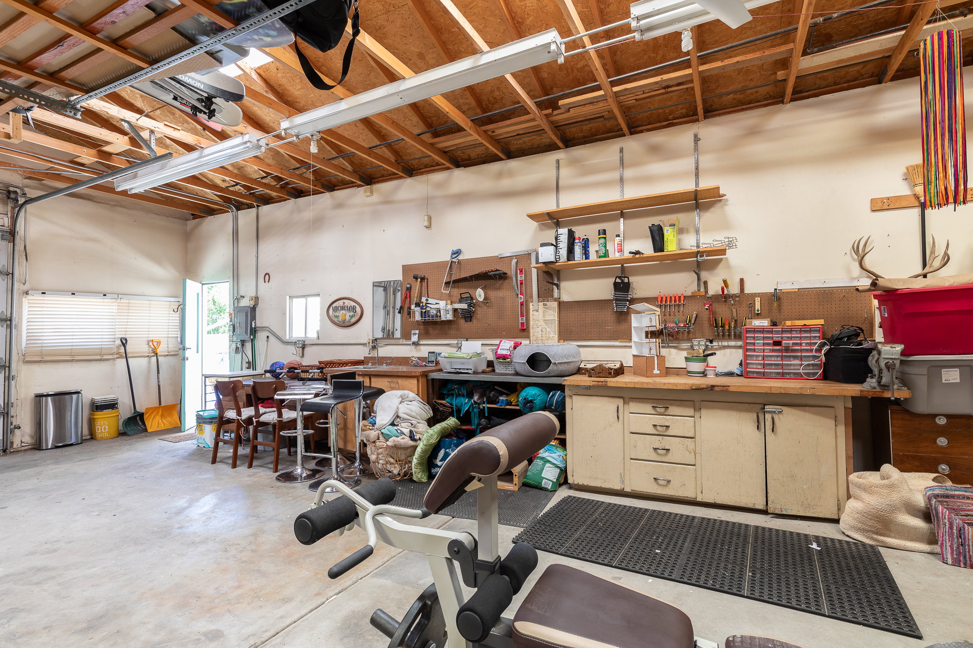 Expansive garage space featuring exposed wood beam ceiling, concrete flooring, and a workbench with built-in cabinetry