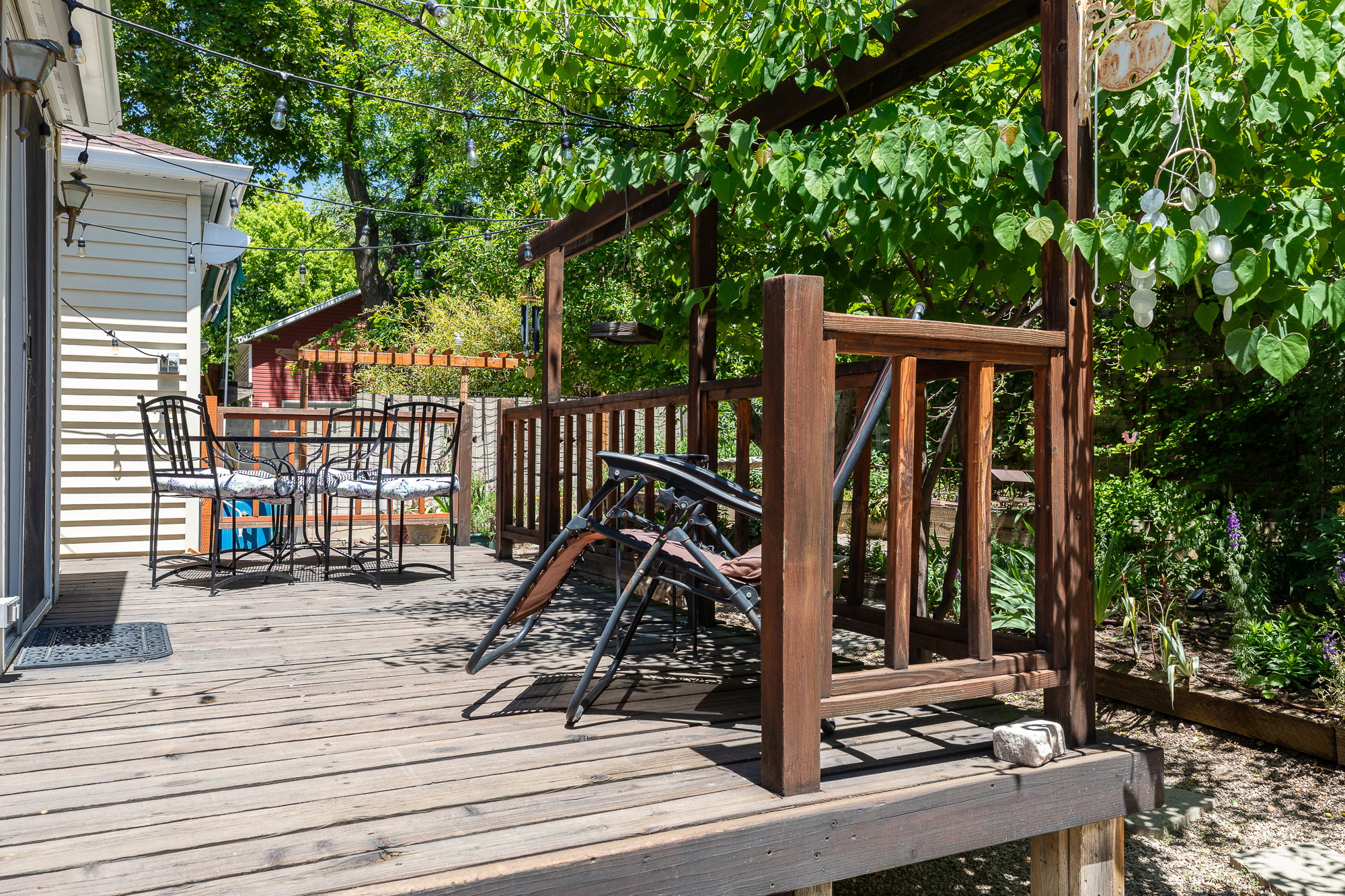 Spacious wood-finish deck with a pergola structure, surrounded by mature greenery and featuring a privacy railing