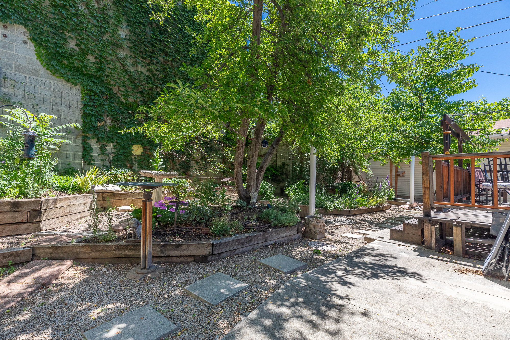 Backyard space featuring a gravel and concrete patio, mature trees, and raised garden beds