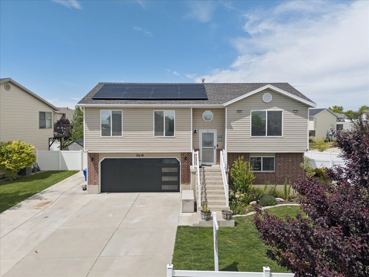 Split-level residence featuring a two-car garage with modern frosted glass panels, an extended concrete driveway, and solar panels