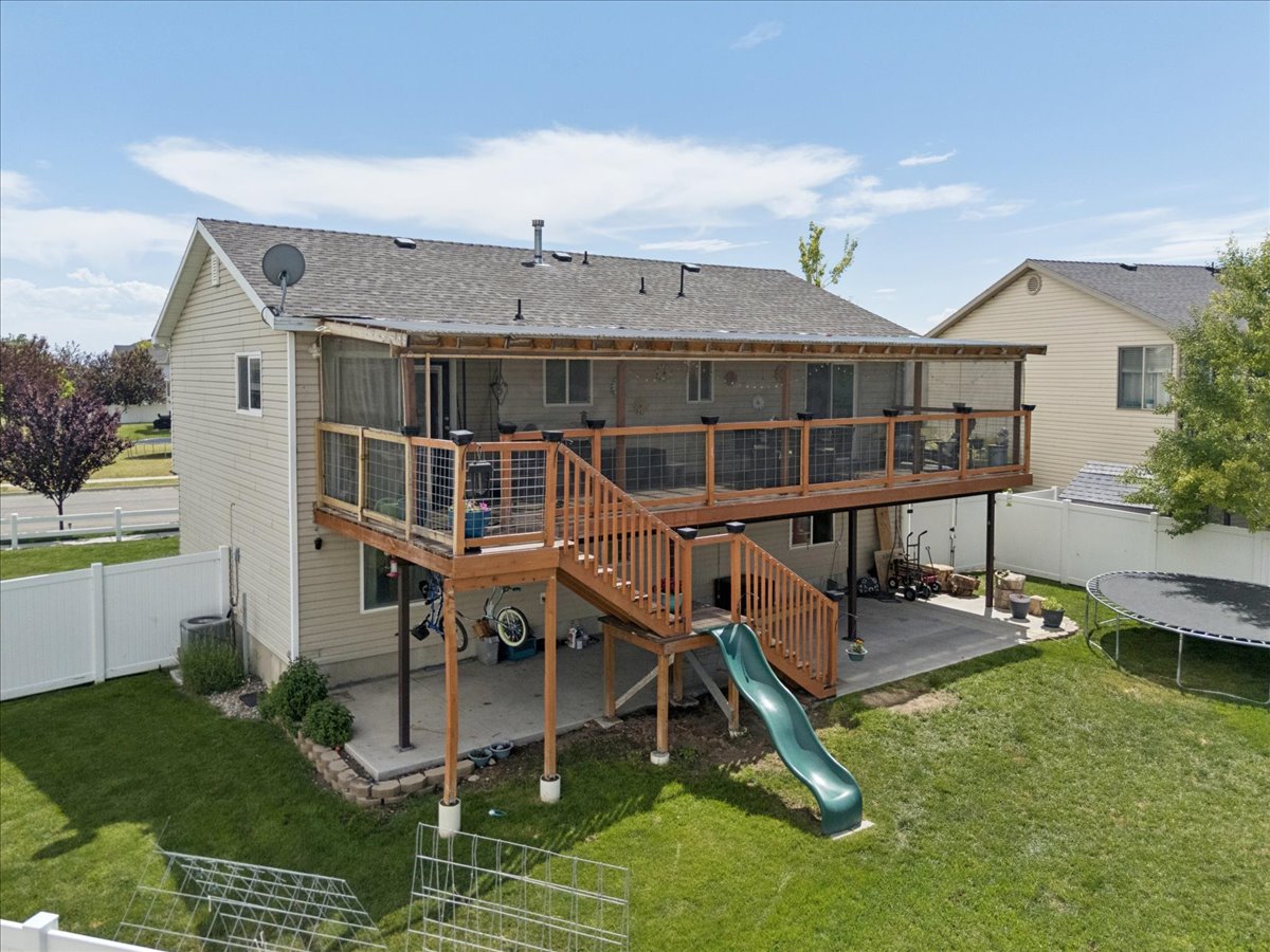 Rear exterior featuring a screened-in deck with wood railing and stairs, a lower concrete patio, and a fenced yard with established landscaping