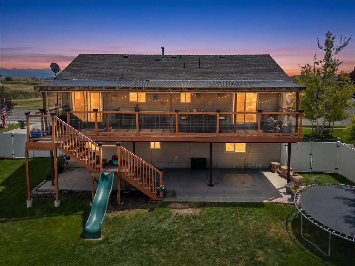 Spacious rear exterior featuring a substantial elevated deck with staircase, ground-level concrete patio, mature green lawn, and full privacy fencing