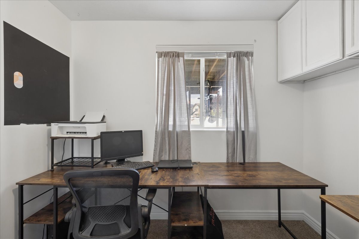Dedicated office space featuring a window with natural light, wall-mounted cabinetry, and a textured carpeted floor