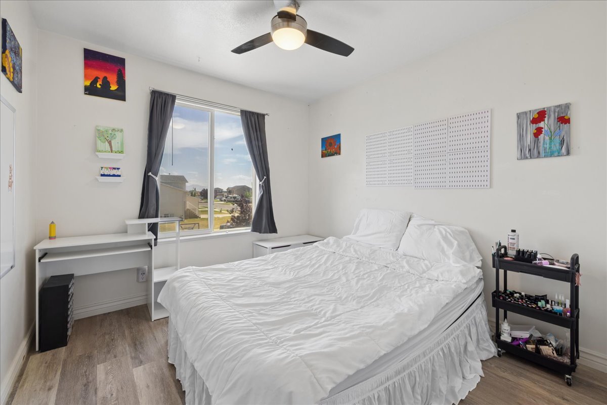 Bedroom featuring wood-finish flooring, a ceiling fan with integrated lighting, and a large window with privacy coverings
