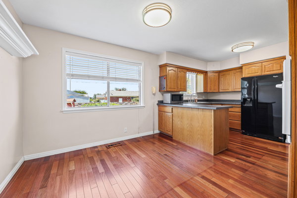 Open-concept kitchen and dining area featuring wood-finish flooring, a kitchen island with dark countertops, oak cabinetry, and a double-pane window with blinds
