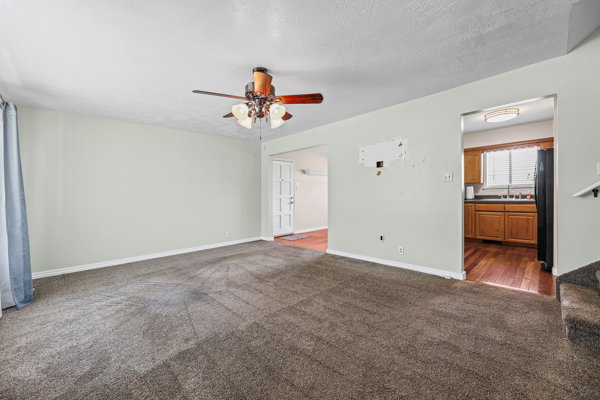 Spacious room featuring gray wall-to-wall carpeting, a ceiling fan with integrated lighting, and light-toned walls