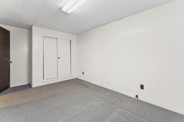 Room featuring light gray carpet, white painted walls, white trim, a built-in closet with sliding doors, and an overhead fluorescent light fixture