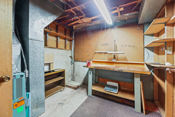 Utility room featuring a built-in workbench, pegboard wall, built-in shelving, concrete flooring, and exposed ceiling joists