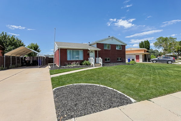 Brick-front residence featuring a covered carport, concrete driveway, and a front yard with manicured lawn and decorative landscaping