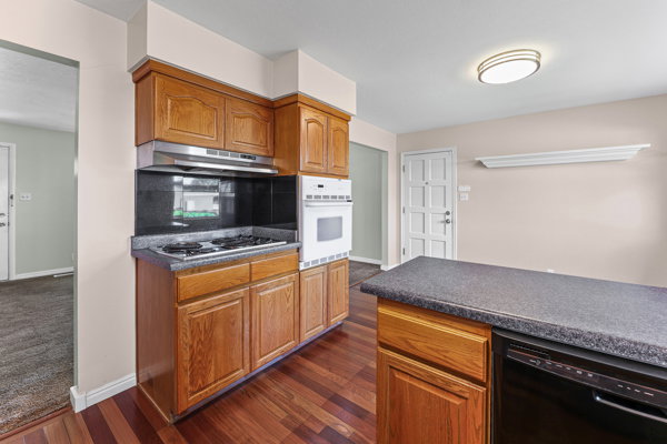 Kitchen featuring wood cabinetry, dark countertops, a built-in oven, and a cooktop with an overhead range hood