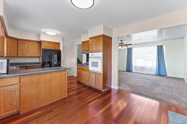 Kitchen featuring wood-finish flooring, oak cabinetry, black appliances, light-toned countertops, and a built-in oven