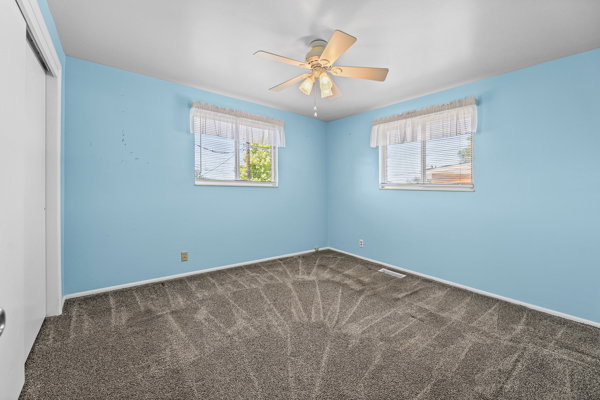 Room featuring two windows with horizontal blinds, a ceiling fan, and grey patterned carpeting