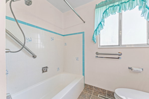 Full bathroom featuring a white porcelain tub, white tiled shower surround with blue accent trim and floral details, and a chrome showerhead with a flexible hose