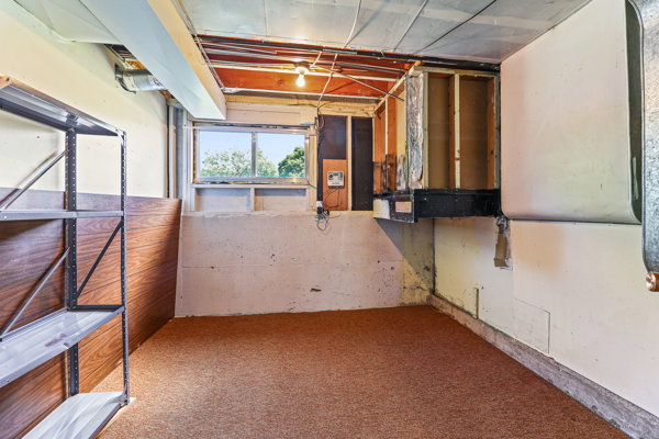 Basement space featuring a window, exposed ceiling joists, and a partial wood-finish wall