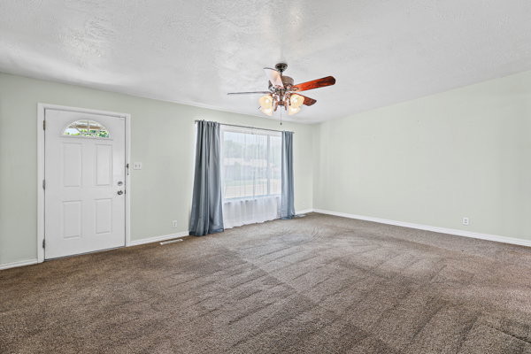 Spacious interior room featuring light-colored walls and brown carpeting