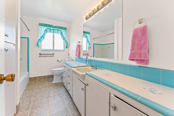 Bathroom featuring a single window, white vanity with integrated sink, tiled countertop, and matching tiled backsplash