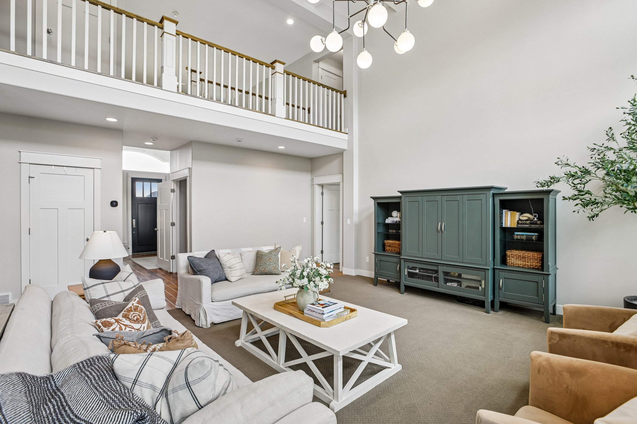 Vaulted ceiling living area featuring a second-story interior balcony with white balusters and wood-finish handrail, a contemporary multi-orb chandelier, and recessed lighting
