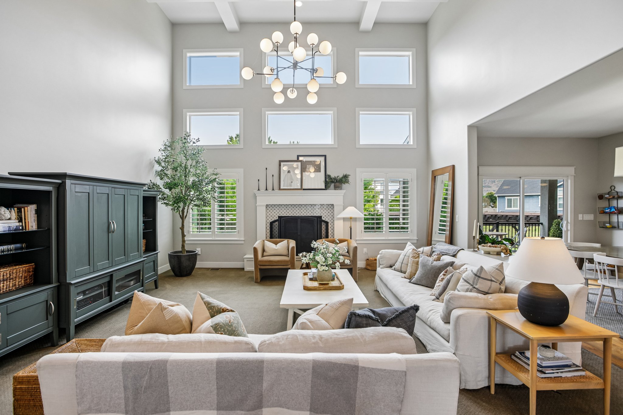 Two-story living area featuring a fireplace with a decorative tile surround and white mantel, a multi-pane window configuration, white window shutters, a contemporary chandelier, and recessed lighting