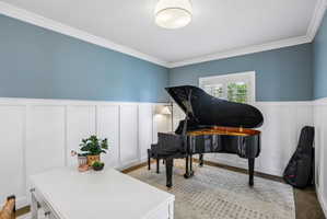 Room featuring a combination of board and batten paneling and painted walls, crown molding, a window with exterior views, and a flush-mount ceiling light fixture