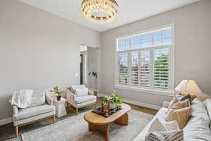 Living area featuring high ceilings, a prominent chandelier, and a large window with plantation shutters