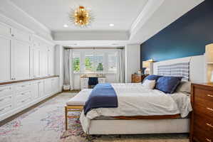 Recessed ceiling with a modern light fixture, extensive white built-in cabinetry with wood-finish countertops, custom window shutters, and a contrasting accent wall