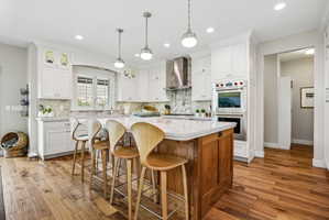 Kitchen featuring a large central island with seating, white cabinetry, integrated stainless steel appliances, wood-finish flooring, and pendant lighting