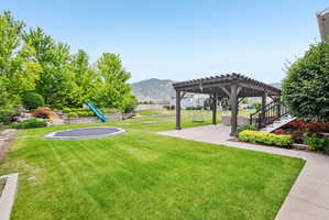 Expansive backyard featuring a large green lawn, concrete patio, and a dark wood pergola