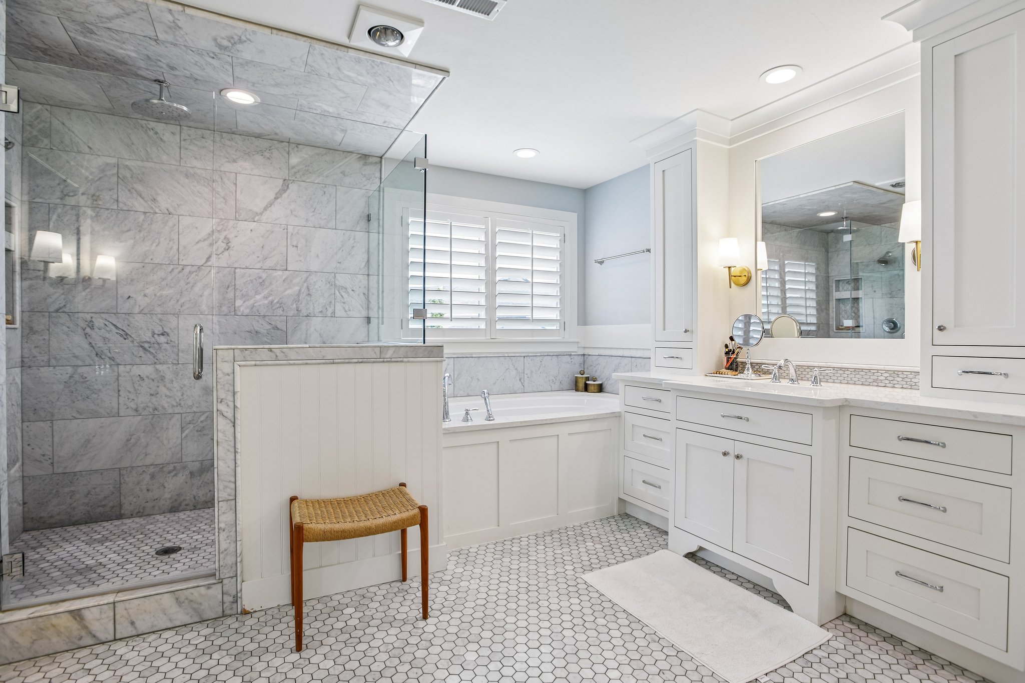 Bathroom featuring a frameless glass shower enclosure with tiled walls, a built-in soaking tub, extensive white cabinetry with integrated storage, dual sinks, and white hexagonal floor tiling