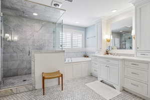 Bathroom featuring a frameless glass shower enclosure with tiled walls, a built-in soaking tub, extensive white cabinetry with integrated storage, dual sinks, and white hexagonal floor tiling