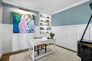 Interior room featuring board and batten paneling, crown molding, a built-in bookcase with integrated lighting, and wood-finish flooring