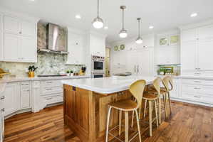 Spacious kitchen featuring a wood-finish island with seating, white shaker cabinetry, herringbone tile backsplash, integrated appliances, and wood-finish flooring