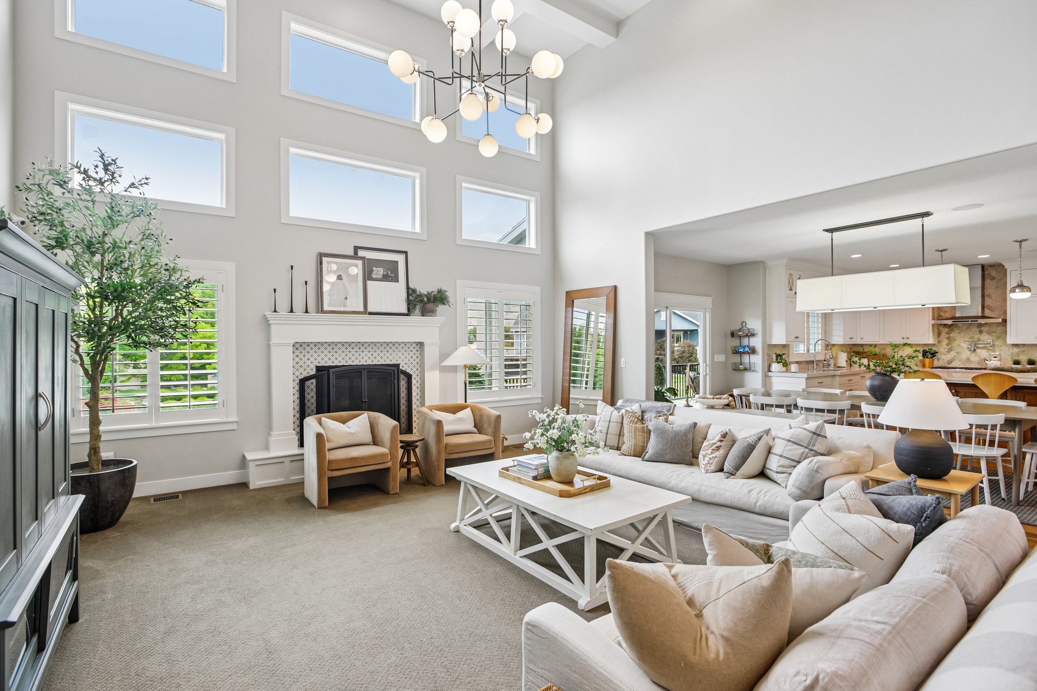Double-height living space featuring extensive upper-level transom windows, a central chandelier, and a fireplace with a decorative tile surround and mantel