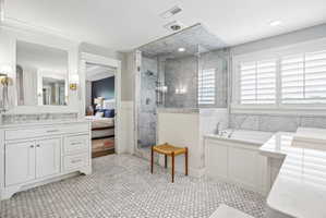 Bathroom featuring white hexagon tile flooring, a glass-enclosed shower with tiled walls, a separate soaking tub with a tiled surround, white vanity cabinetry with a stone countertop, and plantation shutters