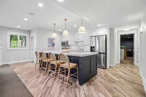 Kitchen featuring a dark-toned island with a light-colored countertop, three pendant lights, stainless steel appliances, white cabinetry, and wood-finish flooring
