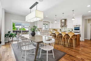 Open-concept kitchen and dining area featuring wood-finish flooring, white cabinetry, a kitchen island with seating, stainless steel appliances, and sliding glass doors opening to an outdoor deck