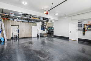 Spacious garage featuring a durable dark flooring finish, extensive built-in wood-finish cabinetry, an integrated utility sink, overhead storage racks, and a white entry door