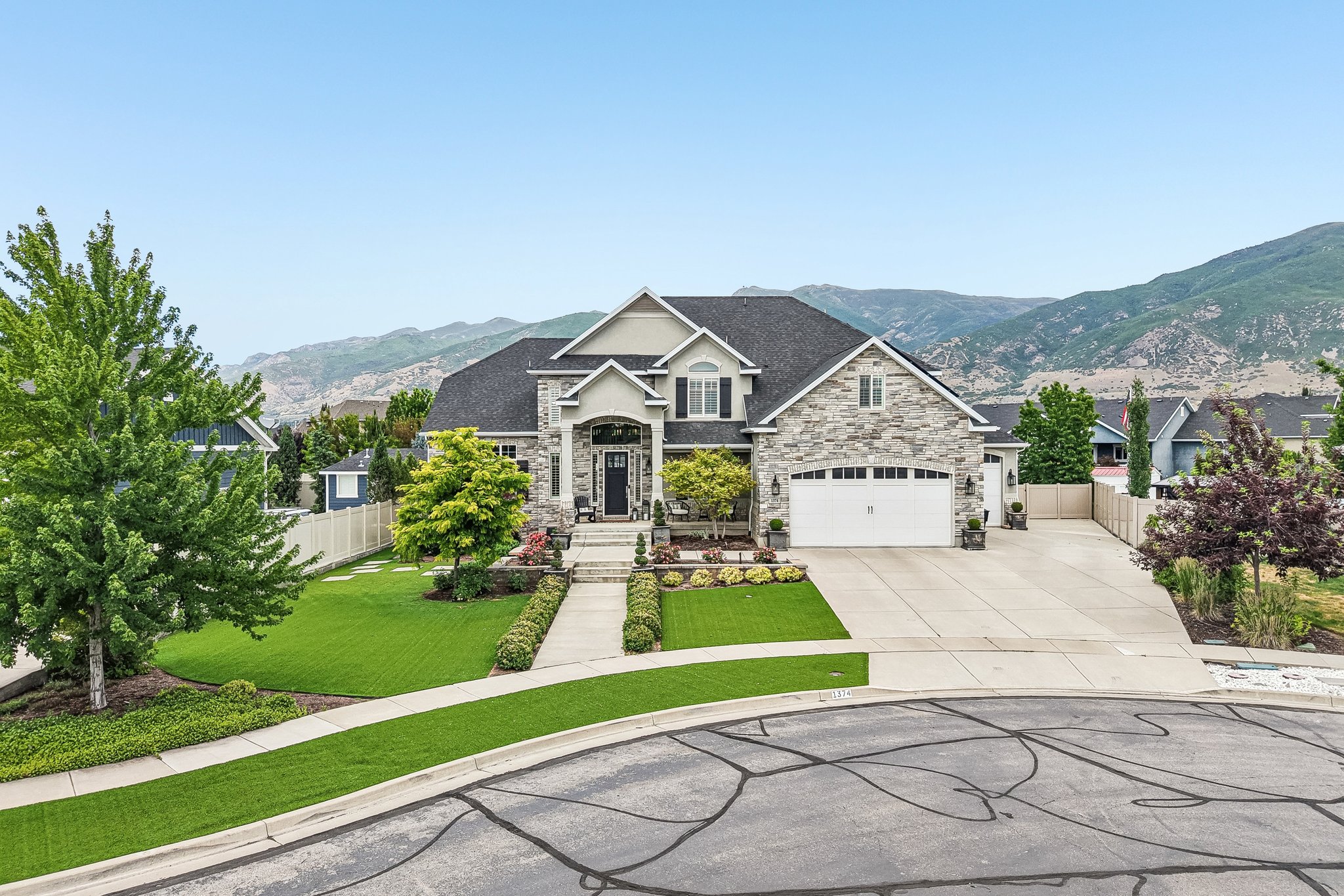 Grand two-story residence featuring a stone and stucco exterior, prominent gable roofs, an attached two-car garage with white panel doors, and a concrete driveway