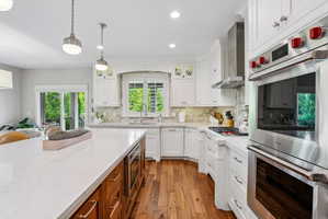 Gourmet kitchen featuring white cabinetry, light countertops, wood-finish flooring, a built-in double oven, and stainless steel appliances