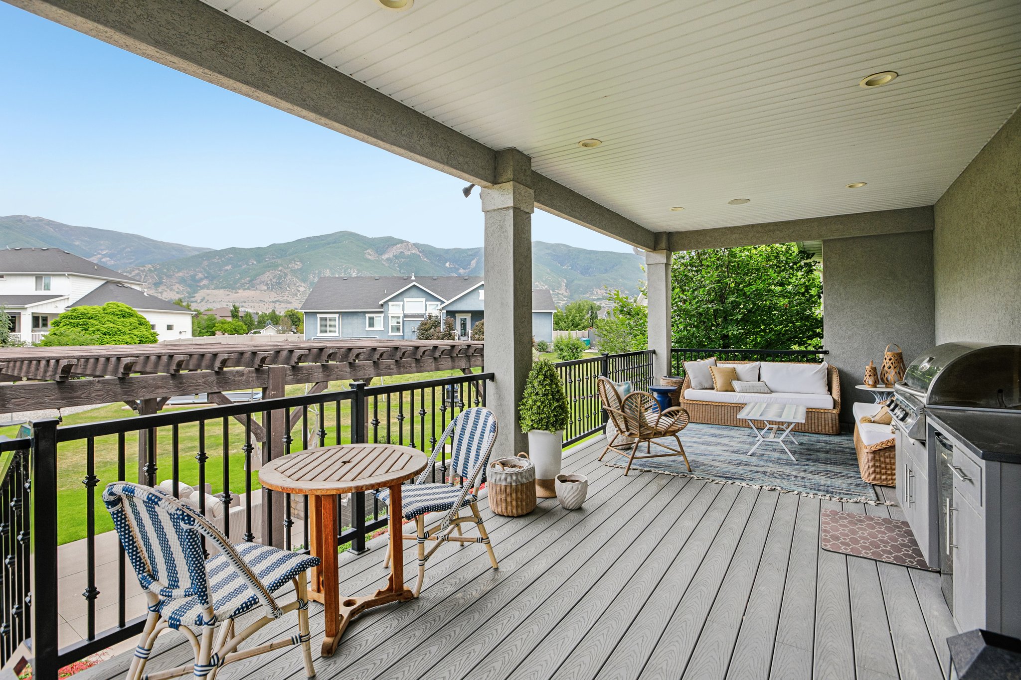 Expansive covered deck featuring composite decking, recessed lighting, a built-in outdoor kitchen with grill, and black wrought iron railings