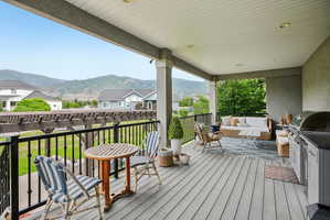 Expansive covered deck featuring composite decking, recessed lighting, a built-in outdoor kitchen with grill, and black wrought iron railings