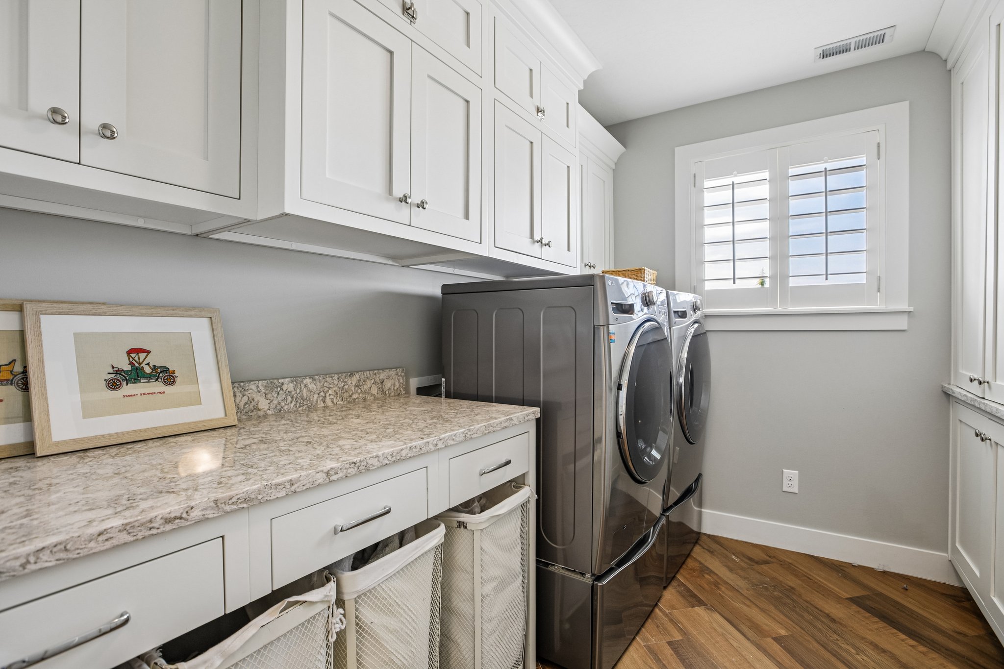 Laundry area featuring wood-finish flooring, white shaker-style cabinetry, and light-toned countertops