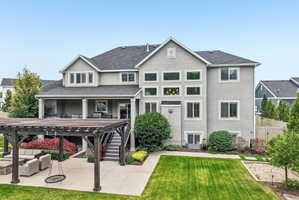 Rear exterior featuring a multi-level stucco facade, covered patio, outdoor pergola, and a manicured lawn
