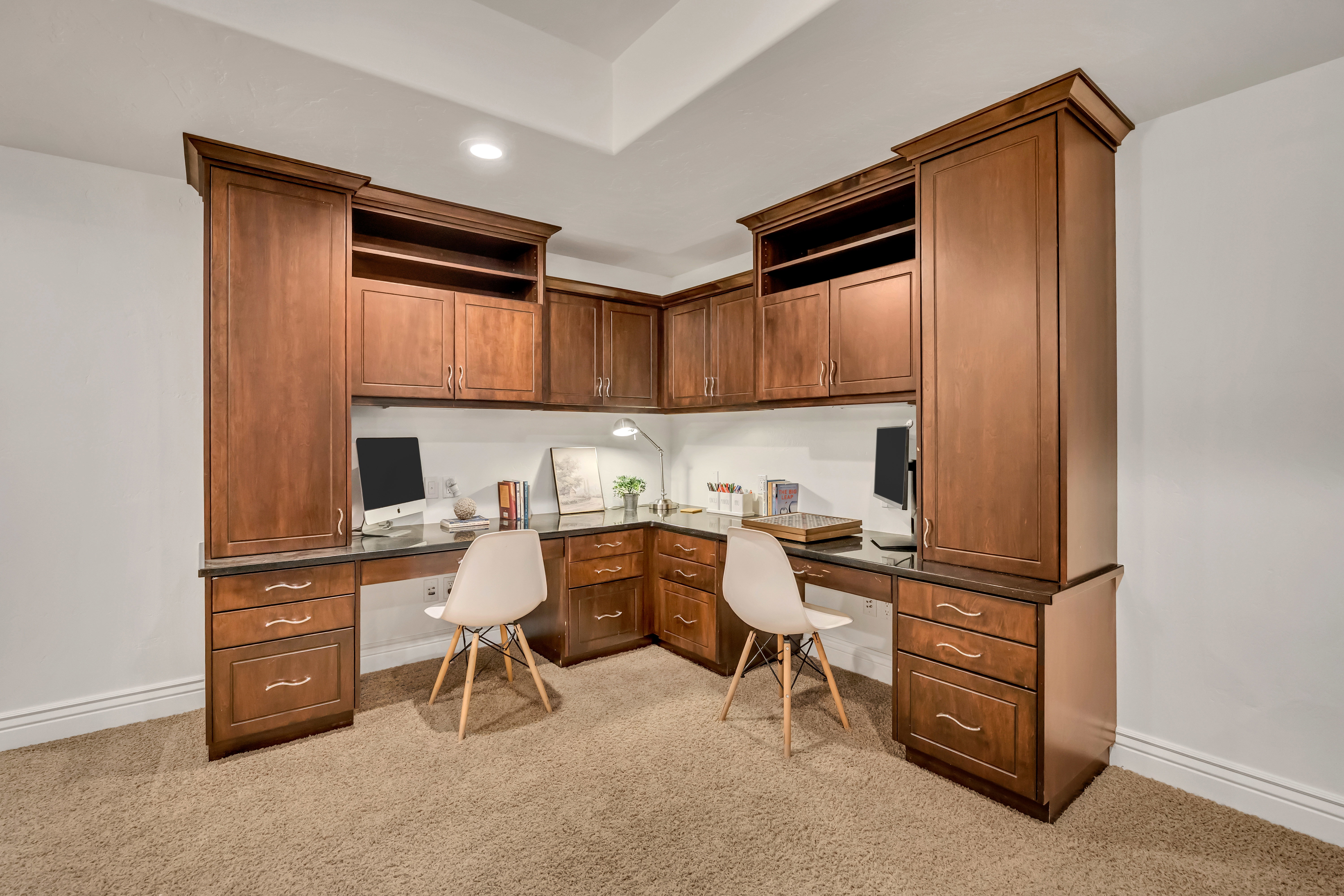 Built-in office space featuring rich wood cabinetry, integrated desks with stone countertops, overhead storage, and recessed lighting