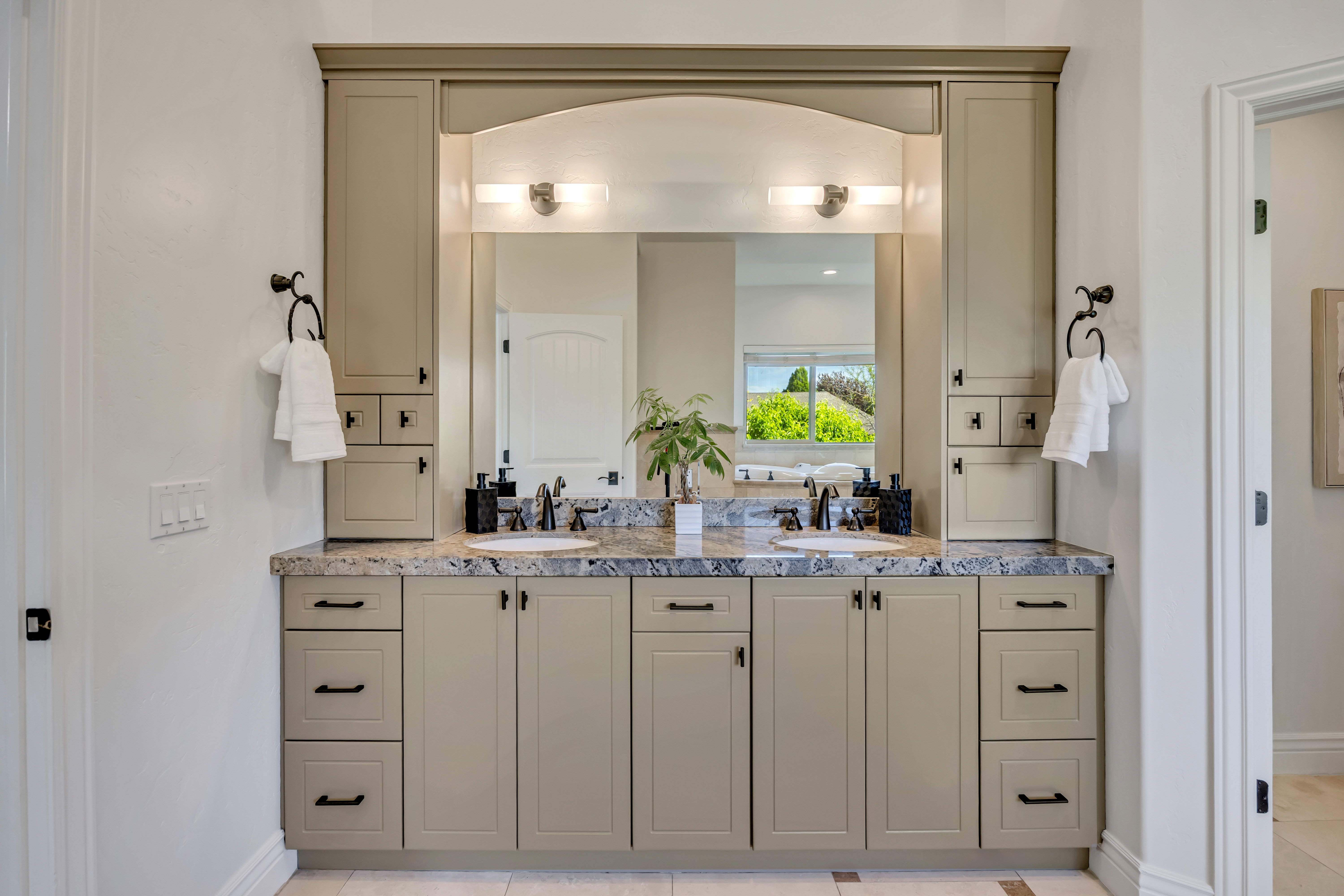 Double vanity featuring two undermount sinks with black fixtures, a stone-finish countertop, and ample cabinetry with black hardware